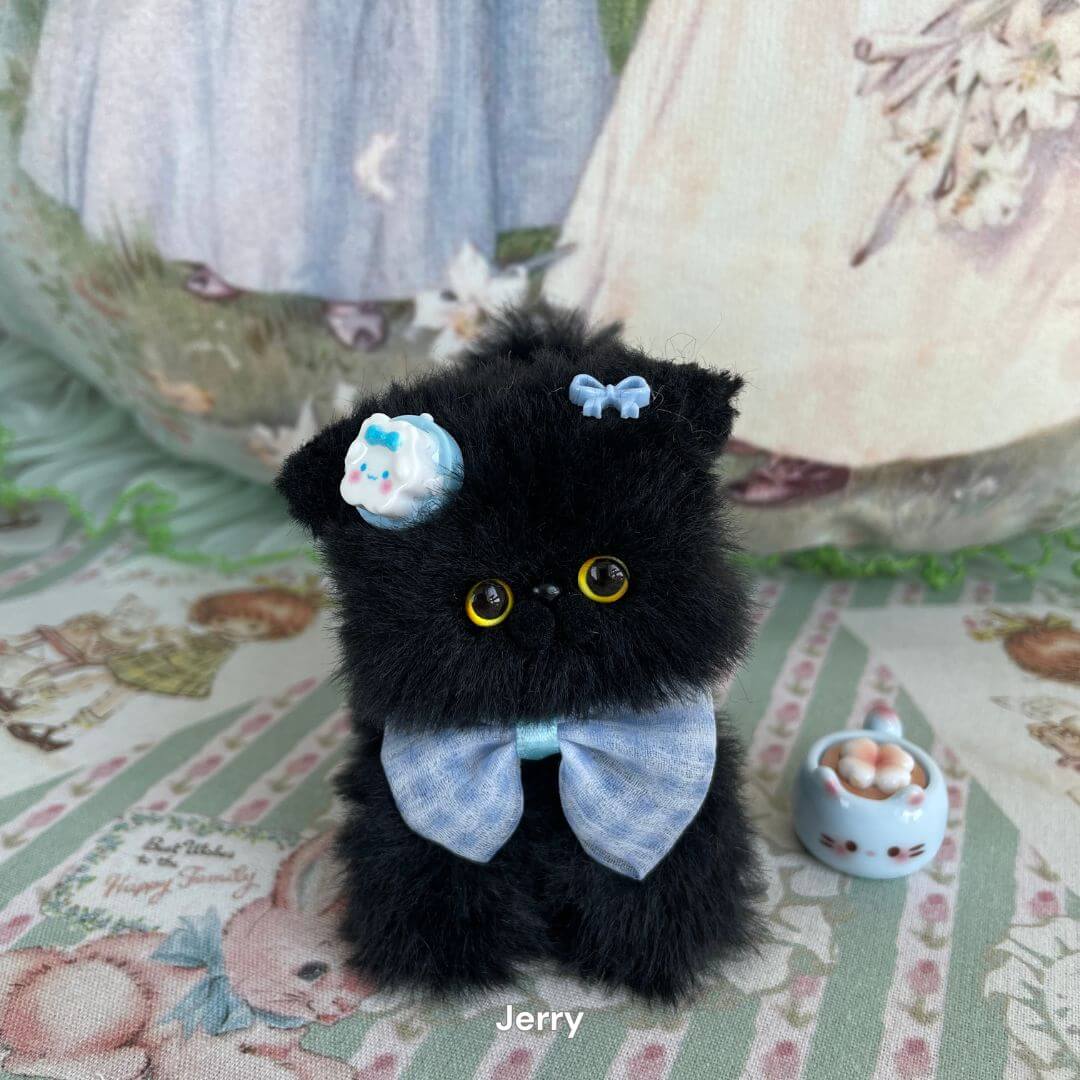 Handmade black faux fur kitten with blue bow and candy accessory from the Black Kitten Collection, displayed on patterned fabric.