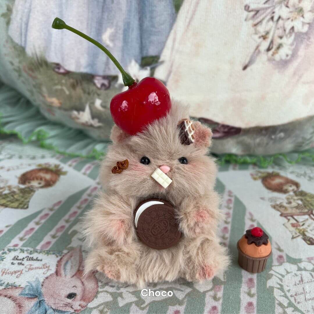 Handmade fluffy hamster with cherry hat, holding cookie, decorated with tiny sweets.