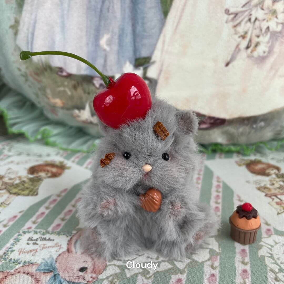 Handmade grey fuzzy hamster with a cherry on top, surrounded by miniature desserts, sitting on a vintage fabric, named Cloudy.