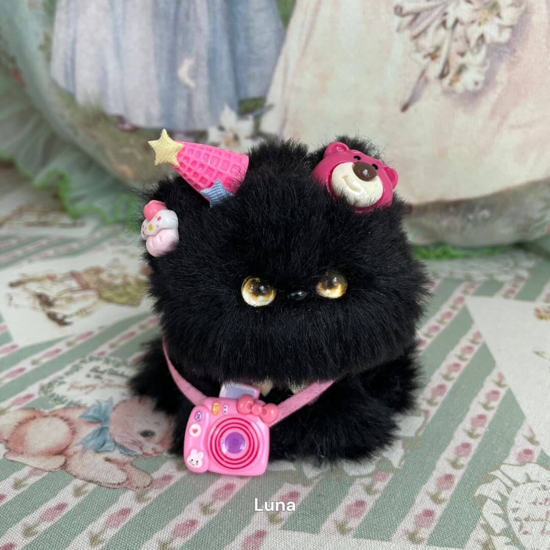 Handmade black kitten plush toy with party hat and pink accessories, part of the Cosplay Kitten Collection, set on a vintage fabric background.