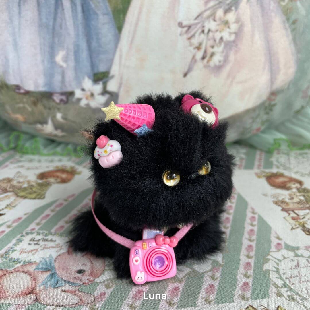 Handmade plush black kitten toy with pink camera charm and colorful accessories, part of the Cosplay Kitten Collection.
