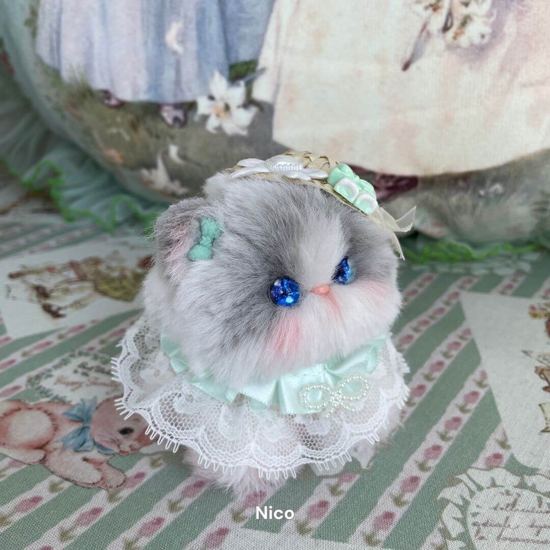 Handmade plush kitten with blue eyes and lace costume from Cosplay Kitten Collection, surrounded by vintage-style decor.