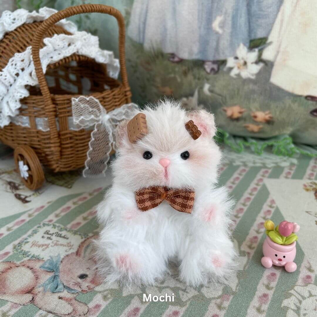 Handmade white plush hamster with bowtie, part of the Adorable Hamsters Collection, next to wicker carriage and small pink accessory.