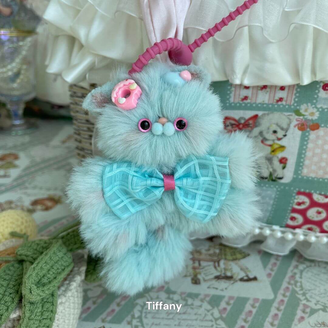 Handcrafted plush kitten pendant with a pastel blue bow and pink accents, ideal as a cute bag charm or keychain accessory.