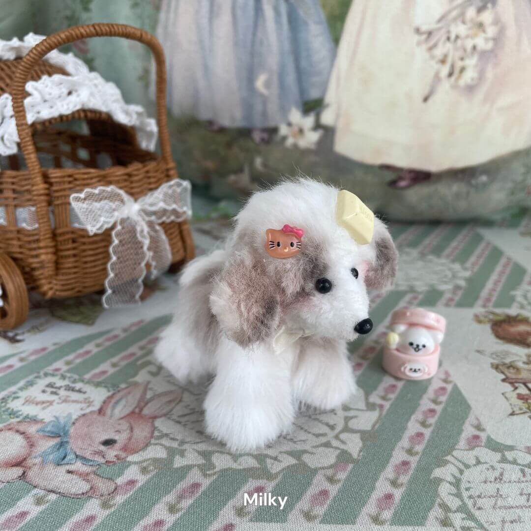 Handmade plush puppy toy 'Milky' with soft faux fur, next to a wicker basket and tiny accessories, on a vintage-themed background