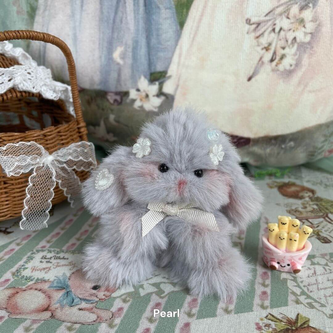 Grey bunny plush with floral decorations and ribbon, part of the Adorable Bunny Collection, seated on patterned fabric with a wicker basket.