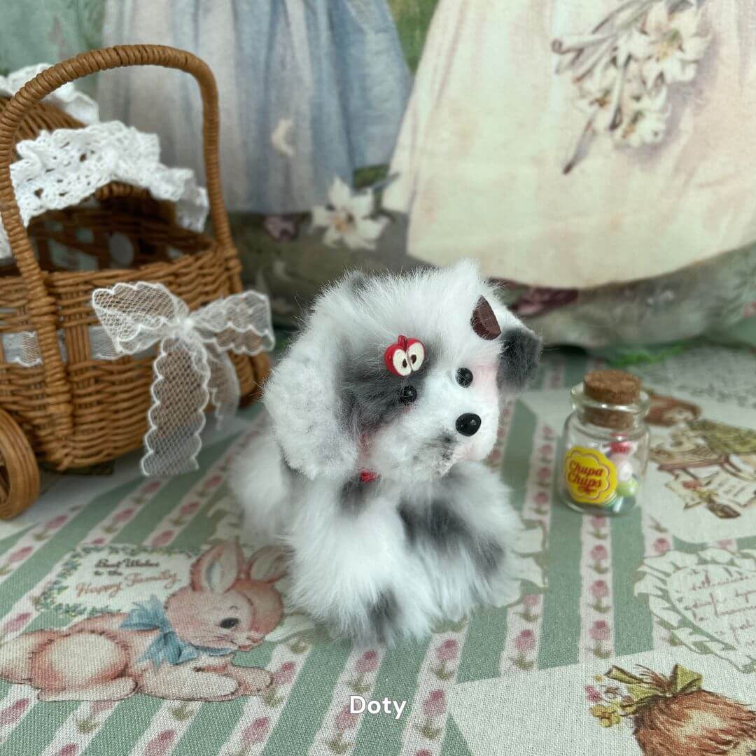 Lifelike hand-sculpted puppy plush toy with soft faux fur, posed on vintage fabric, next to a wicker basket and tiny jar.