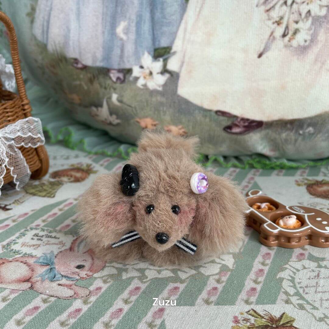 Handmade plush puppy with fluffy fur, adorned with a gem and bow, sitting on a patterned blanket, part of the Adorable Puppy Collection.