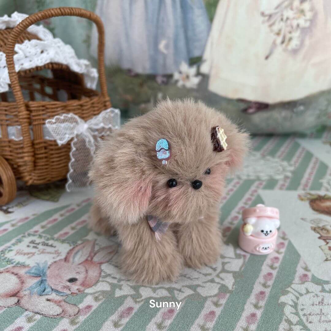 Plush toy puppy named Sunny with mid-length fur and accessories, displayed with a small pink cup on a decorative background.
