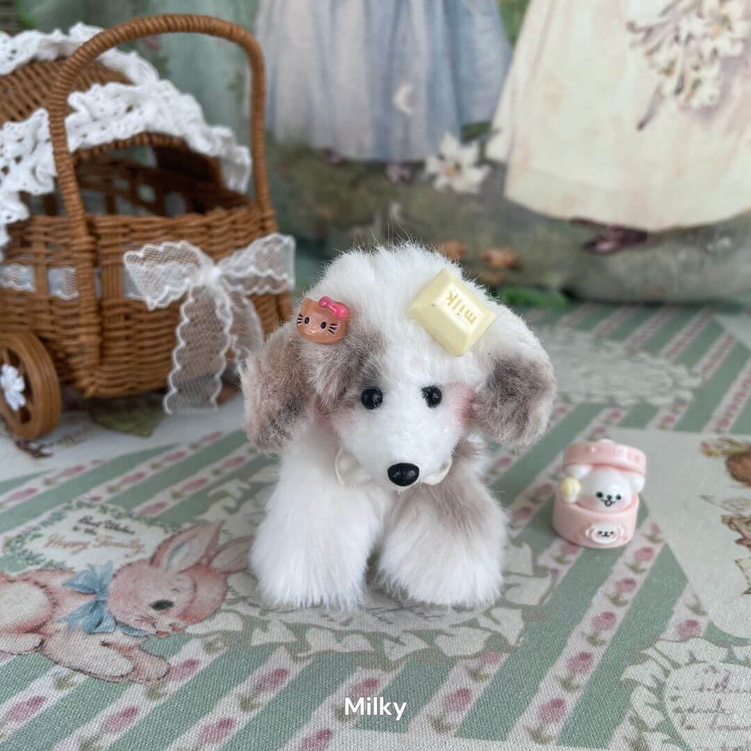 Handmade plush toy puppy 'Milky' with mid-length fur and playful accessories, posing on a patterned background near a wicker basket.