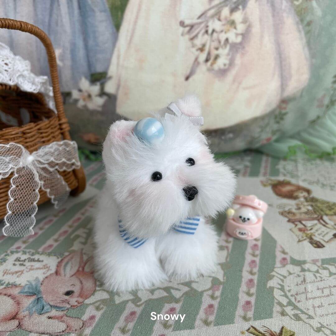 Handmade plush puppy toy named Snowy with white faux fur and a blue bow, set on a decorative mat with vintage designs.