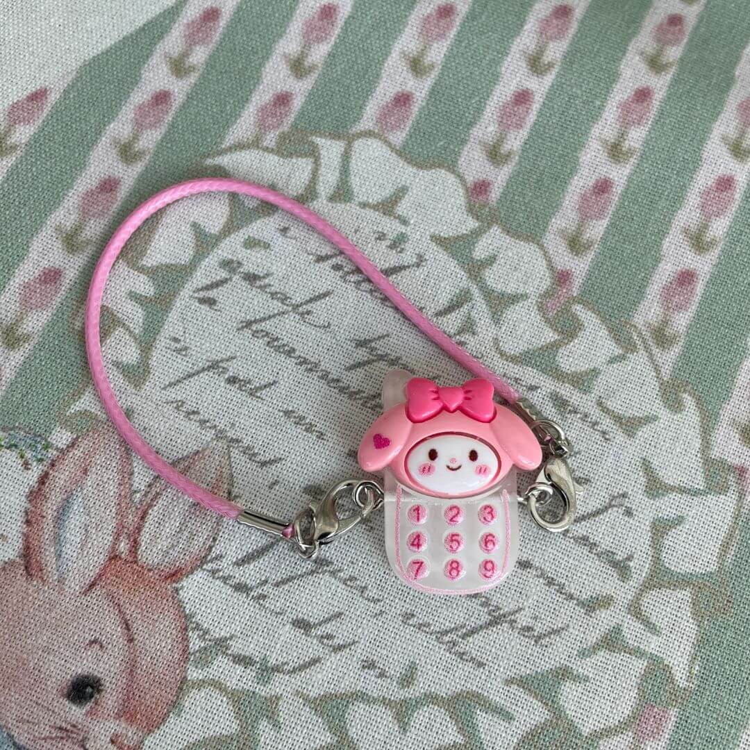 Sanrio character charm with pink phone design, featuring bunny face and dial pad, on decorative background.