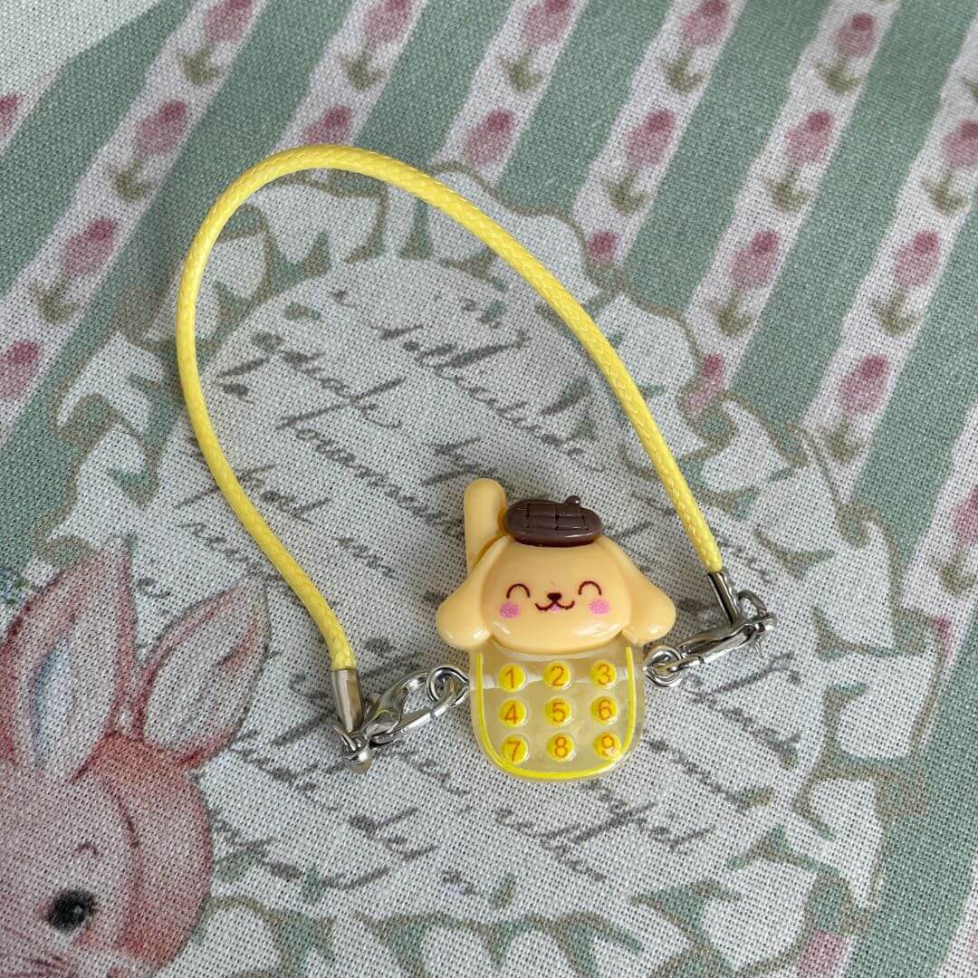 Yellow Sanrio character charm with dial pad, perfect decoration for plush toys or as a cute accessory. Ideal kawaii gift idea.