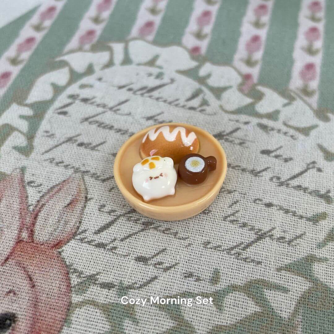 Miniature Cozy Morning Set with pastry, egg, and coffee on printed fabric background.
