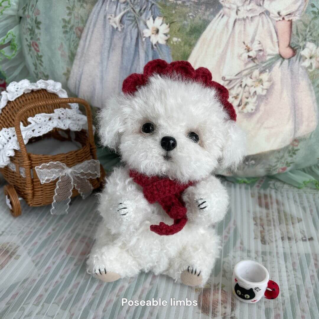 Handmade curly teddy dog with red scarf and head piece, surrounded by mini accessories, created by Anna at Kiki's Handmade Studio.