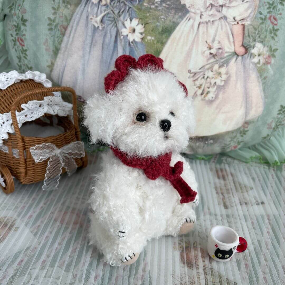 Cuddly Curly Teddy Dog with scarf and lace accessory, sitting beside a wicker stroller and a cup, handmade by Kiki's Studio, 16cm tall.