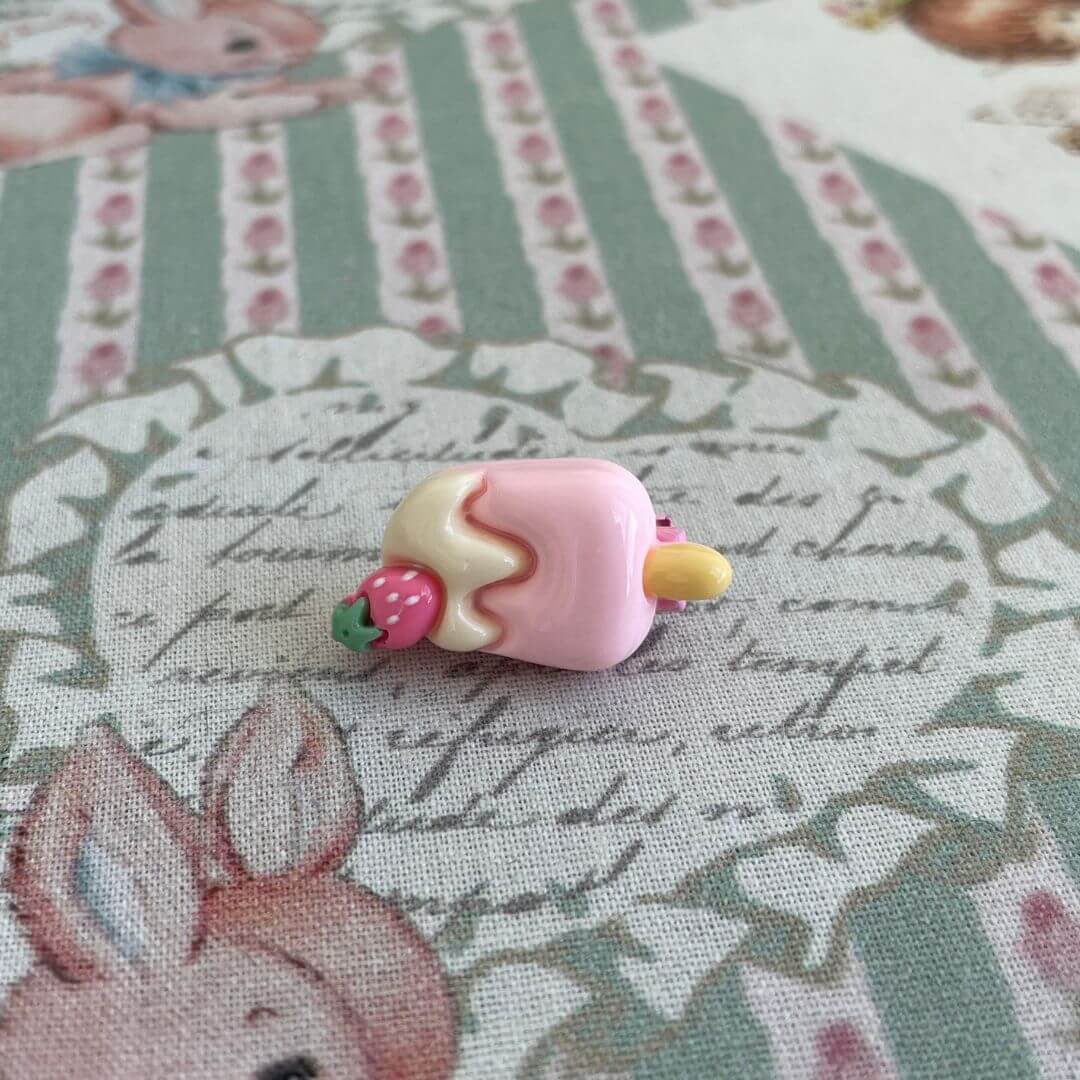Handmade mini clip shaped like a pink cake pop with strawberry detail, perfect as a whimsical accessory for plush toys or clothing.