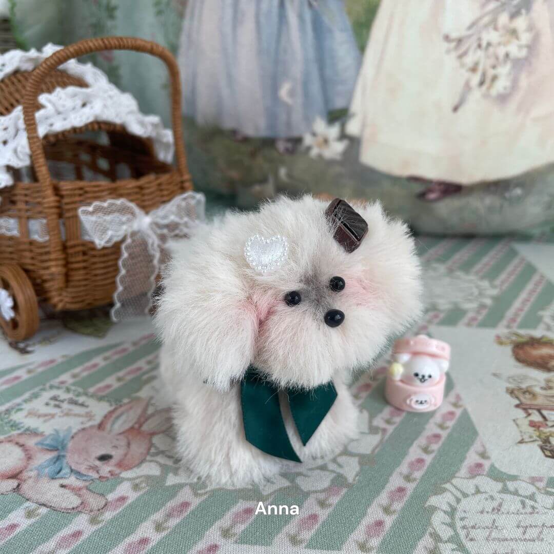 Handmade plush puppy toy with mid-length fur and pearl accessory on decorative table with vintage theme.