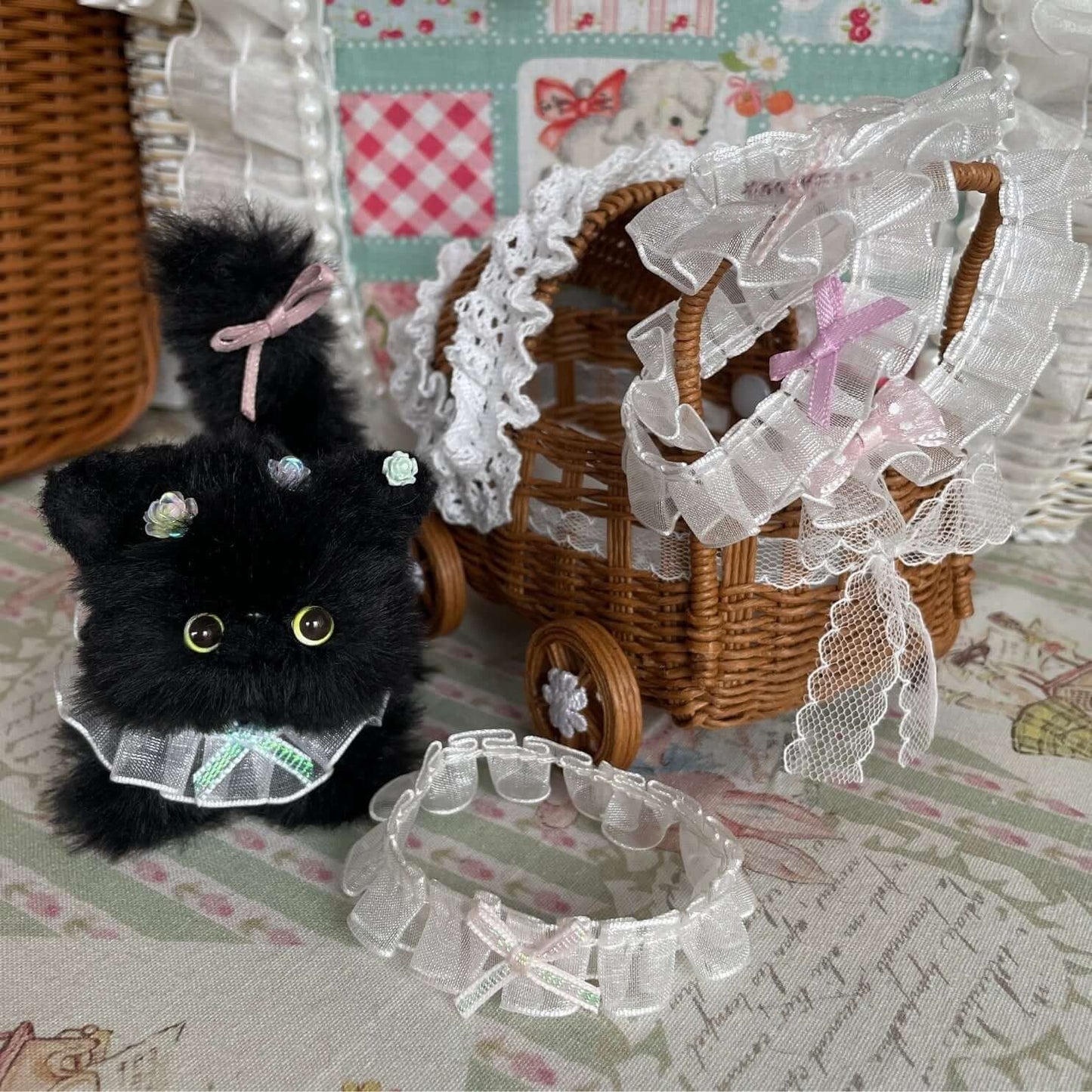 Handmade bow collar on a plush kitten toy beside a lace-decorated wicker cart; collar emphasizes charm in small pets.