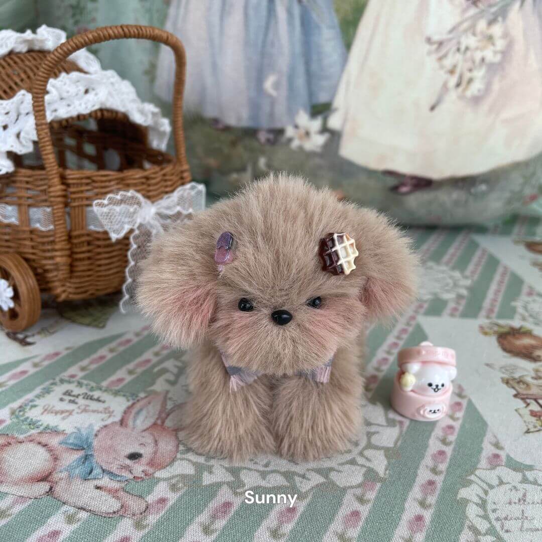 Handmade plush puppy toy Sunny with mid-length fur and cute accessories, displayed on a decorative cloth with a vintage toy pram.