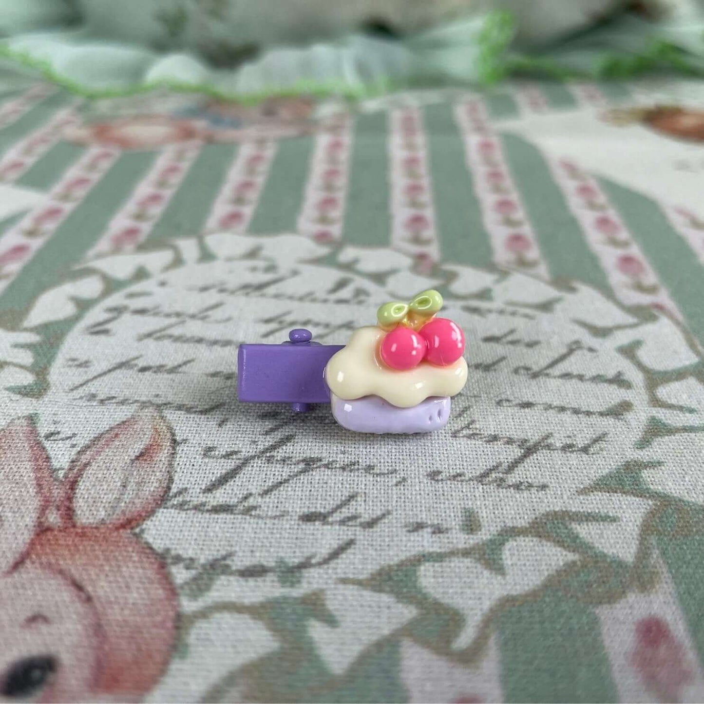 Whimsical cake design handmade mini clip accessory on patterned fabric, perfect for plush toys and decorative use in bags or clothing.
