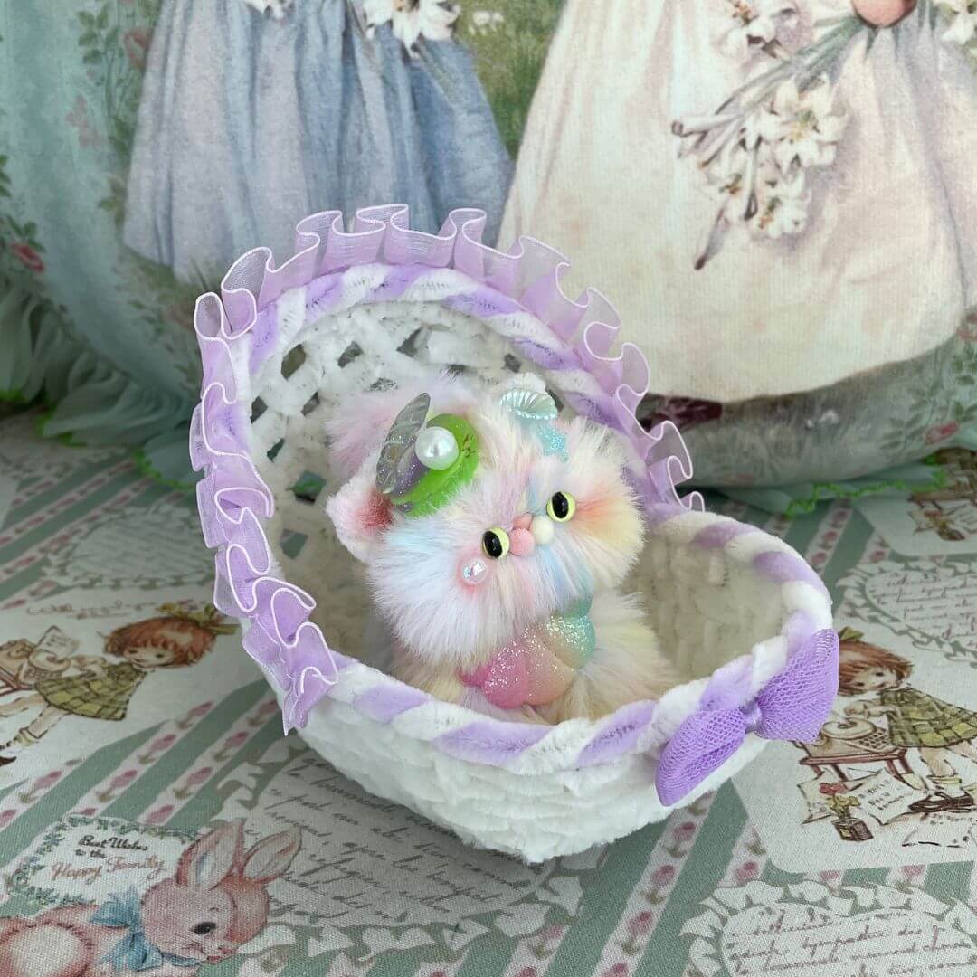 Handmade whimsical cradle with a colorful plush kitten toy, adorned with lavender ruffles and a bow, perfect for miniatures or gifts.