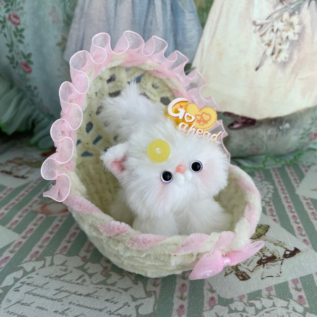 Handmade cradle with plush white kitten, adorned with pink ruffle, perfect for dollhouses or as a charming gift.