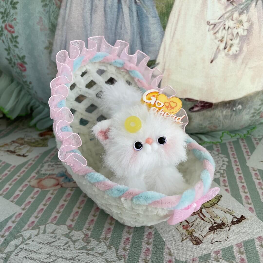 Handmade whimsy cradle with plush kitten toy, featuring a woven design and pastel ribbon trim, perfect for dollhouses or decorations.