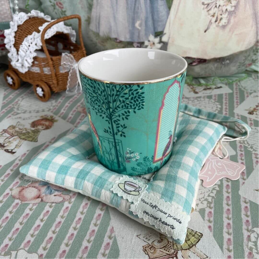 Decorative cup on a kitten-themed handmade coaster on a patterned tablecloth.