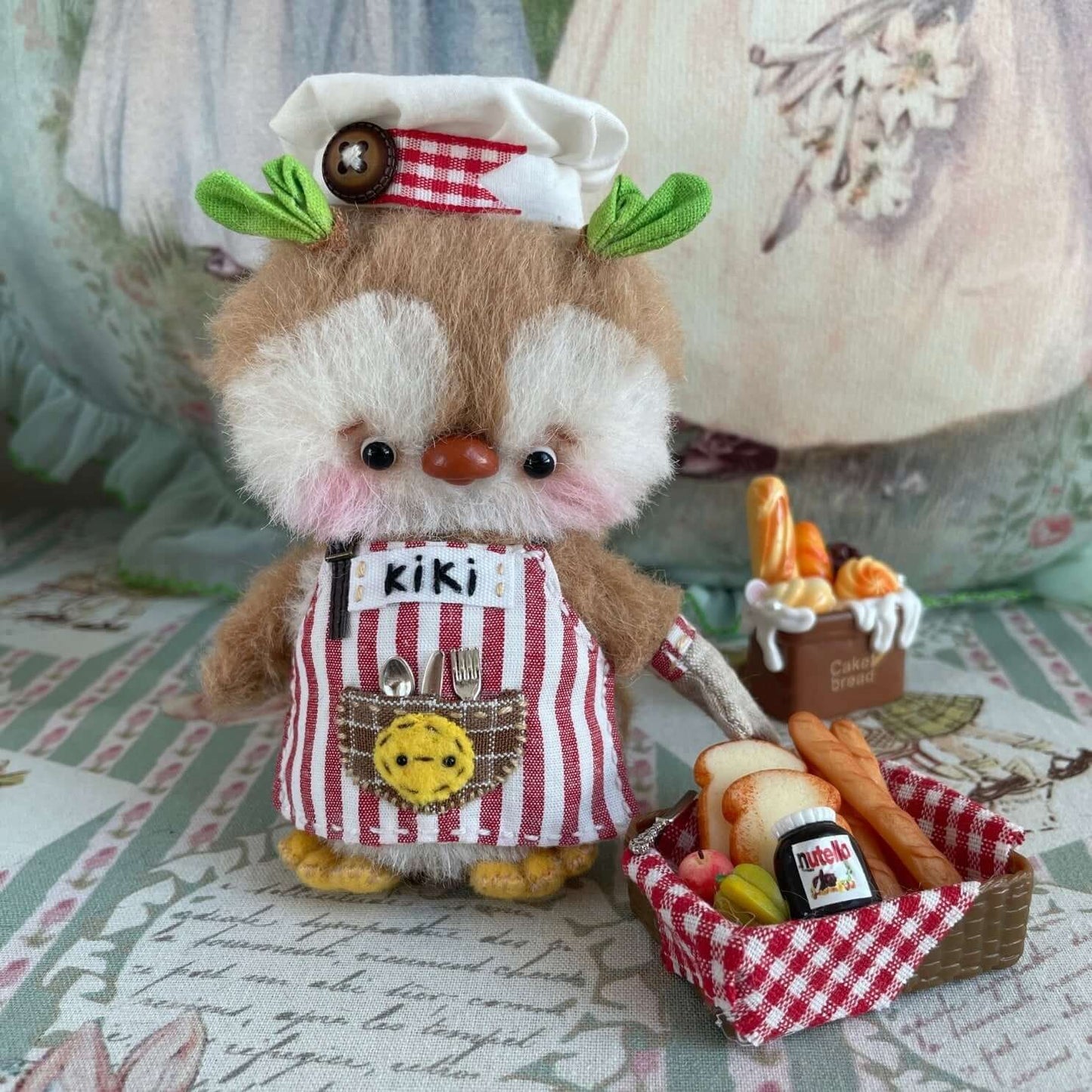 Plush chef penguin with movable joints, wearing a custom apron, hat, and holding baked goods. Handmade by Kiki's Studio.