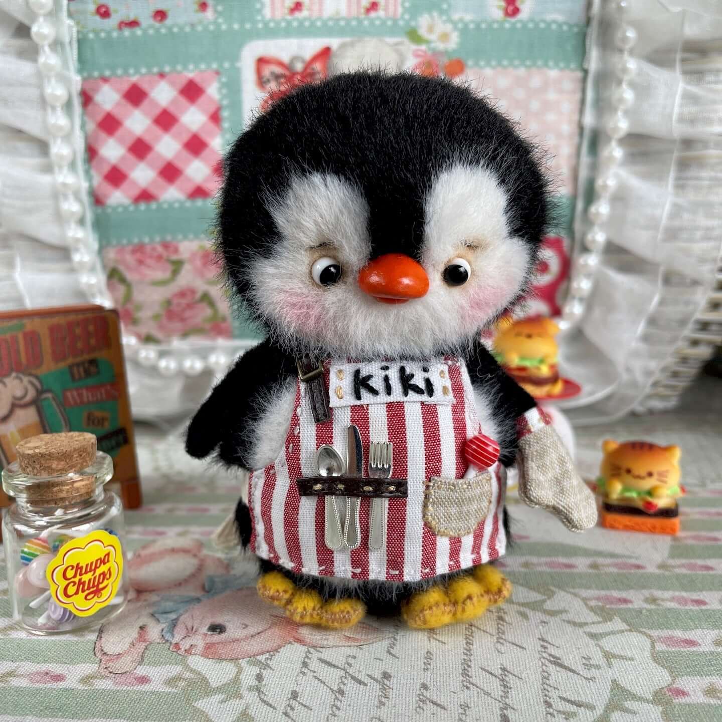 Mini chef penguin plush toy with striped apron, movable joints, and cooking accessories, handmade by René from Kiki's Studio.