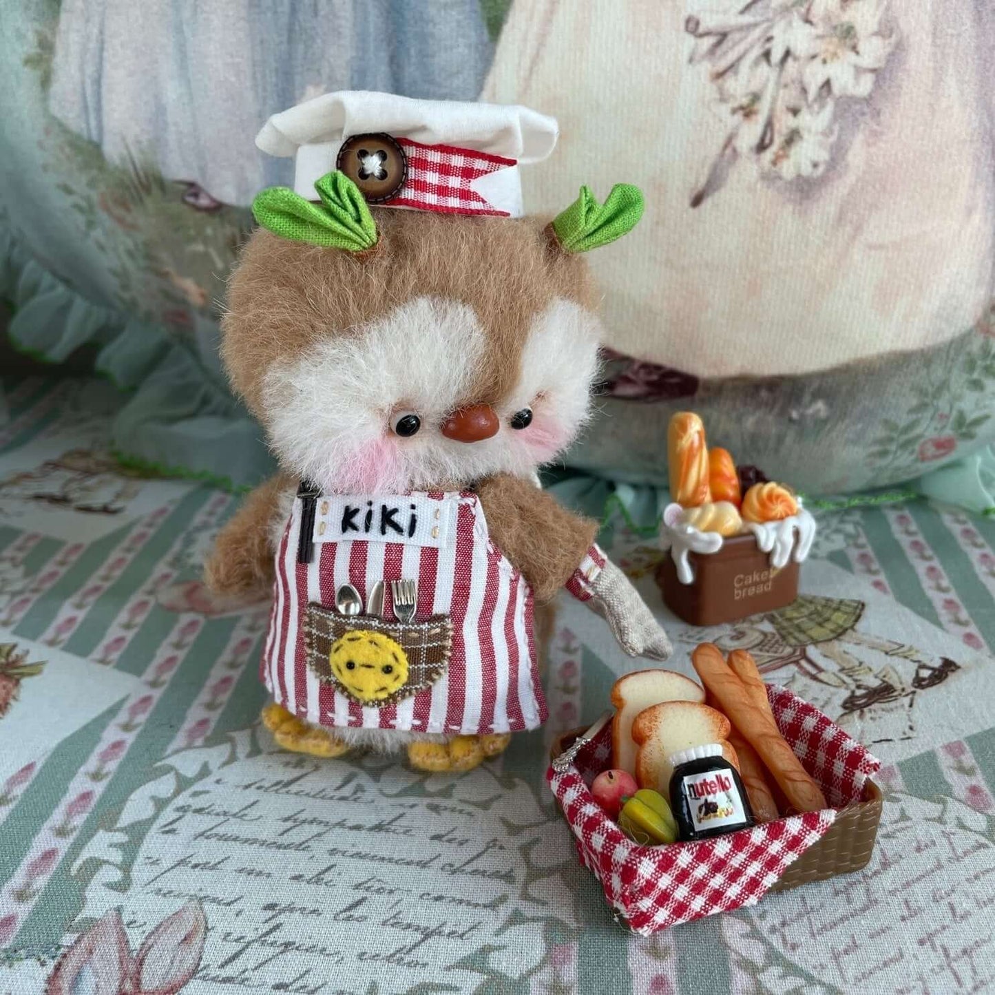 Handmade mini chef penguin toy with movable joints, wearing a custom apron with accessories, displayed on a decorative cloth.