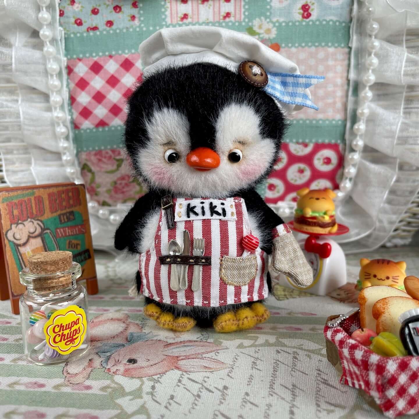 Mini Chef Penguin toy with apron, hat, and glove, set against a colorful background in Kiki's Handmade Studio.
