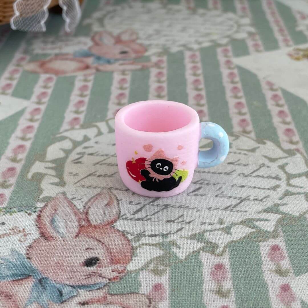 Miniature black kitty cup on a vintage tablecloth, perfect for dollhouse decor or as a gift for cat lovers.