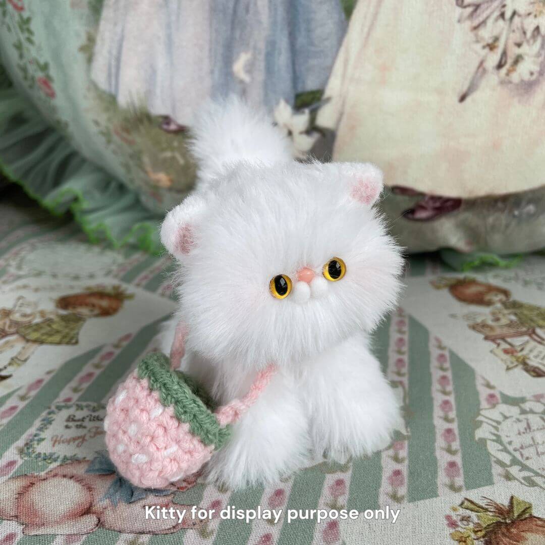 Plush white kitten toy with crocheted pink and green purse on floral background.