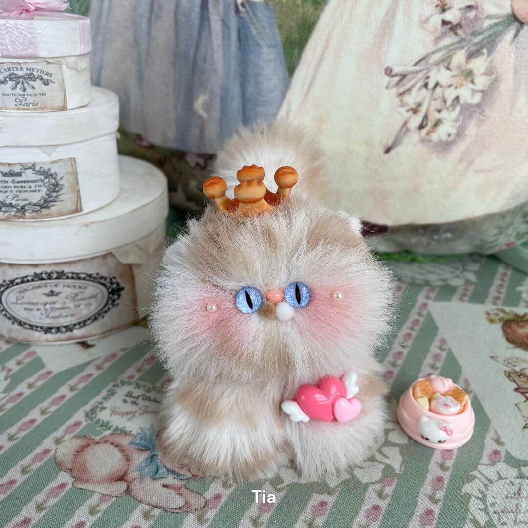 Handmade fluffy kitten plush toy with crown and pink heart, part of the Fluffy Kitten Collection on a decorative background.