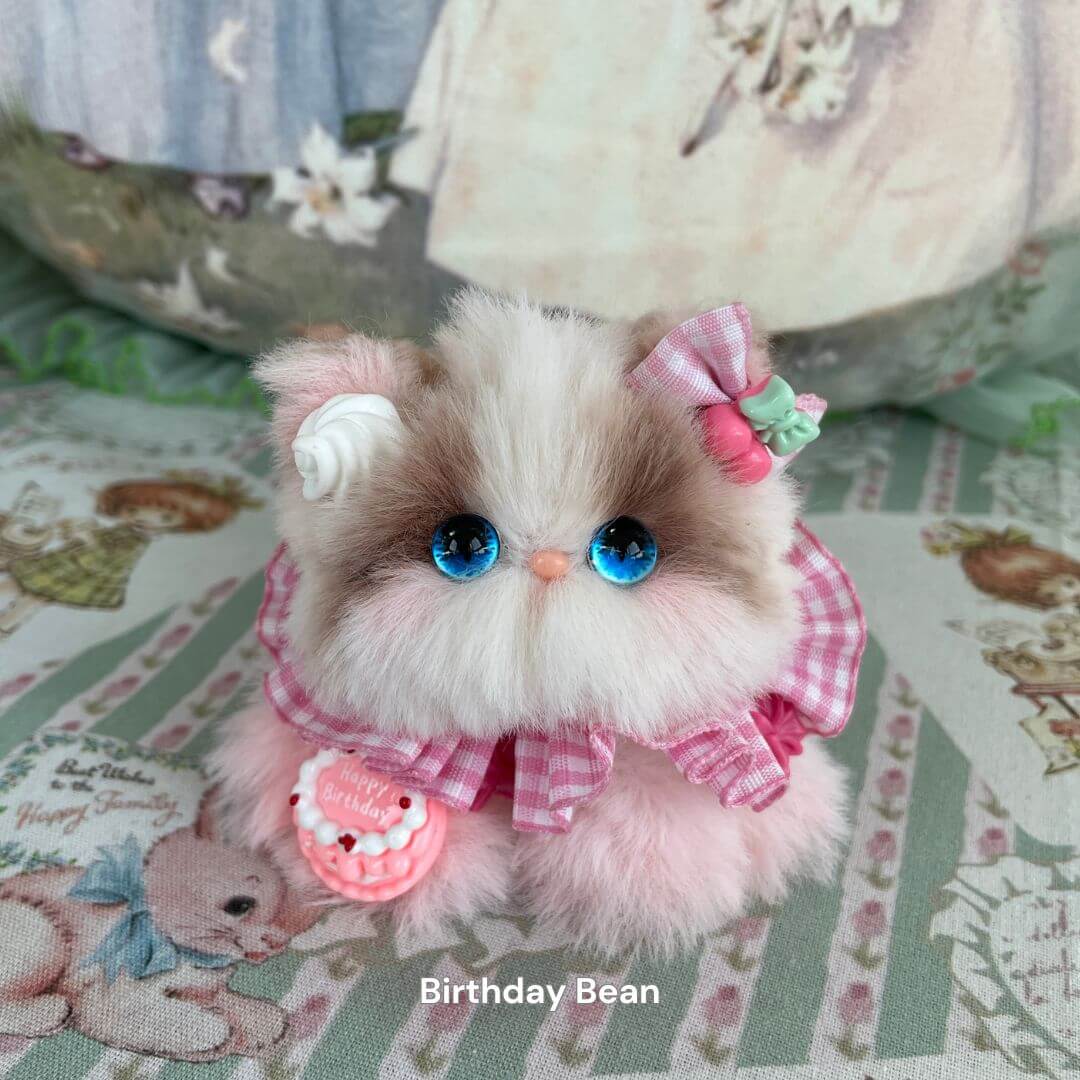 Handmade plush kitten toy from Cosplay Kitten Collection, styled as "Birthday Bean" with a pink gingham dress and decorative bow.