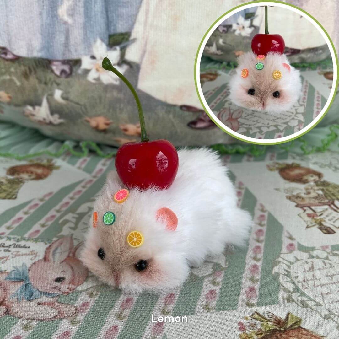 Handmade hamster figurine with faux fur, adorned with a red cherry and candy-like decorations, lying on a patterned surface.