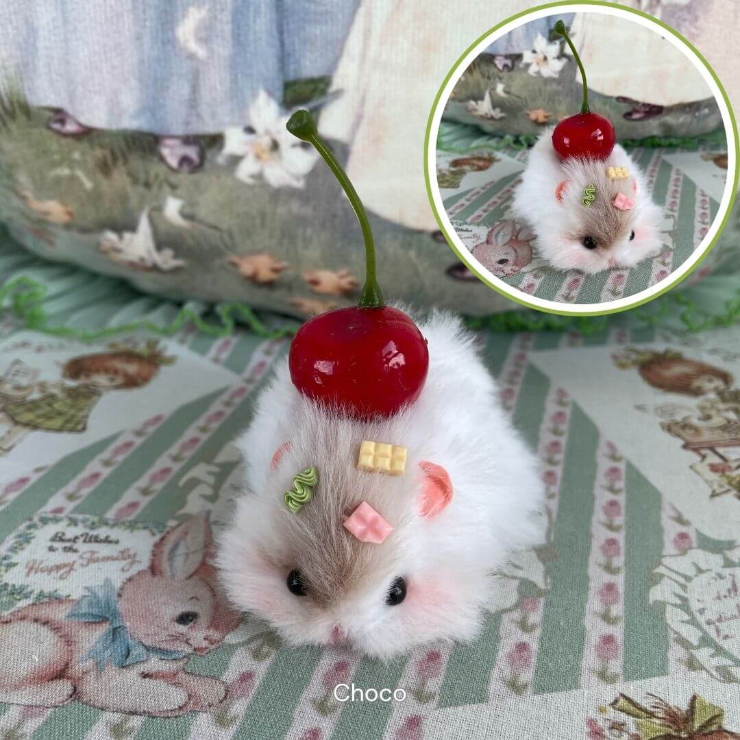 Handmade fluffy hamster figurine lying down with cherry and candy-like decorations, perfect as cute pet accessory or collectible gift.