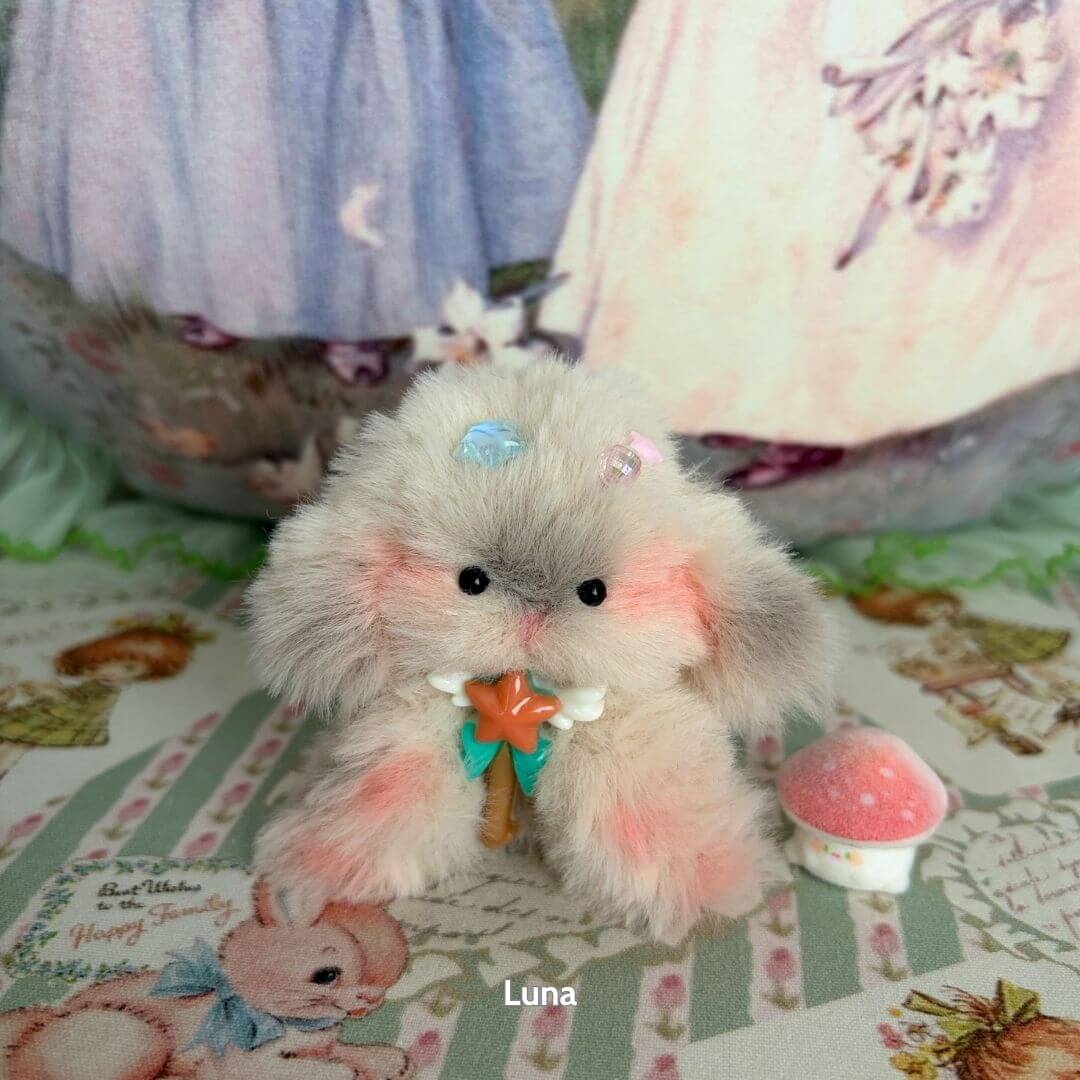 Miniature handmade bunny in soft grey and pink fur, holding a star-shaped candy cane, surrounded by whimsical decor. Adorable Bunny Collection.