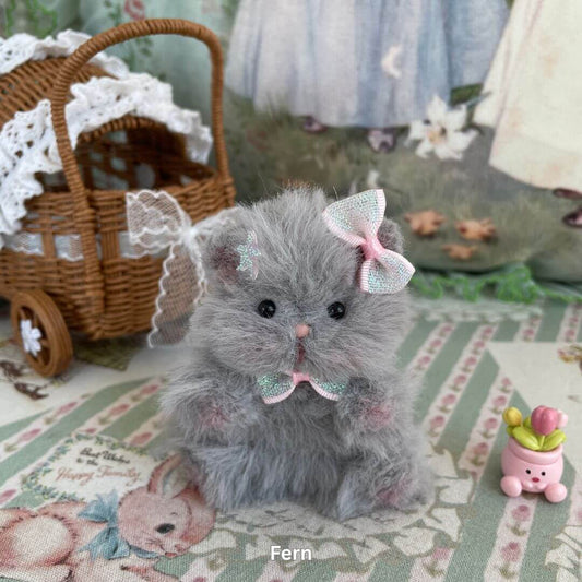 Handmade plush grey hamster with pastel bows, part of the Adorable Hamsters Collection, posed next to a vintage wicker carriage.
