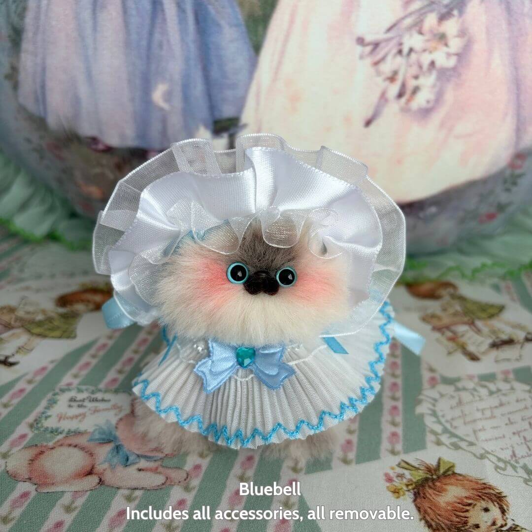 Handmade kitten in a white ruffled dress with blue accents, part of the Petals & Whispers Collection, cute animal collectible.