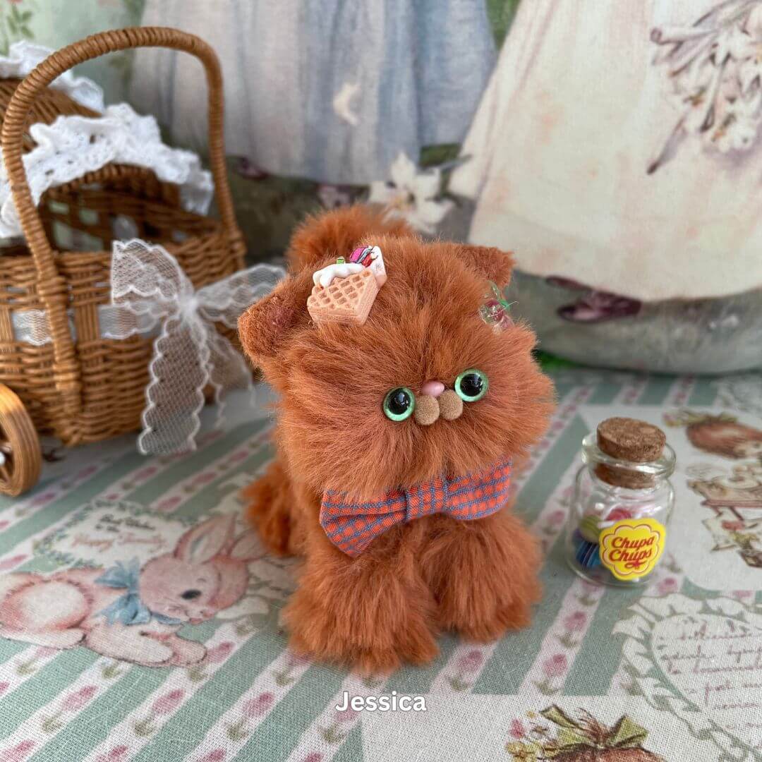 Handmade brown kitten plush toy with waffle accessory, cookie bow, and unique expression on a patterned background.