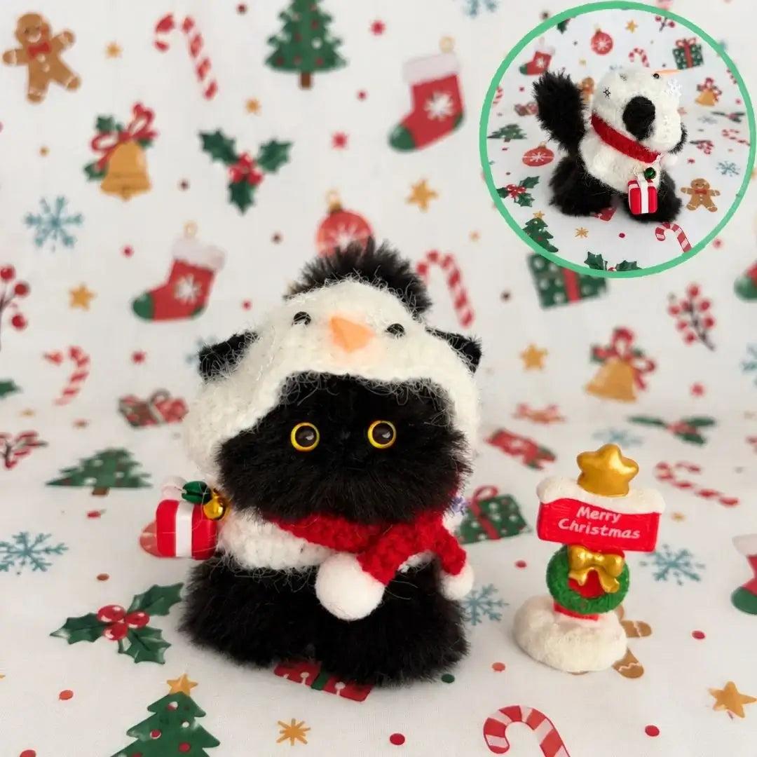 Black kitten wearing a white snowman hat and red scarf.