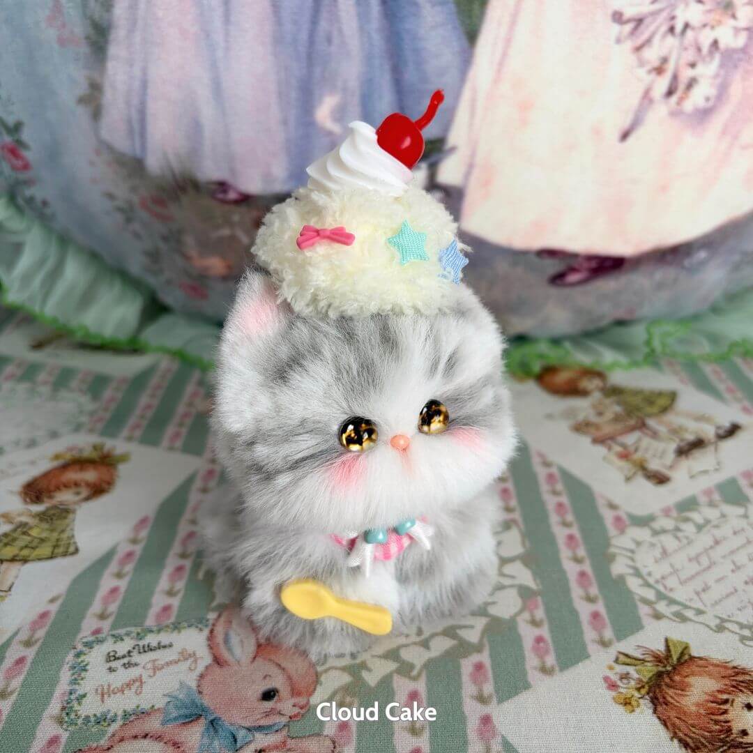 Cute fluffy kitten figurine from the Mewlicious Collection, featuring a grey coat and a cupcake hat with cherry on top.