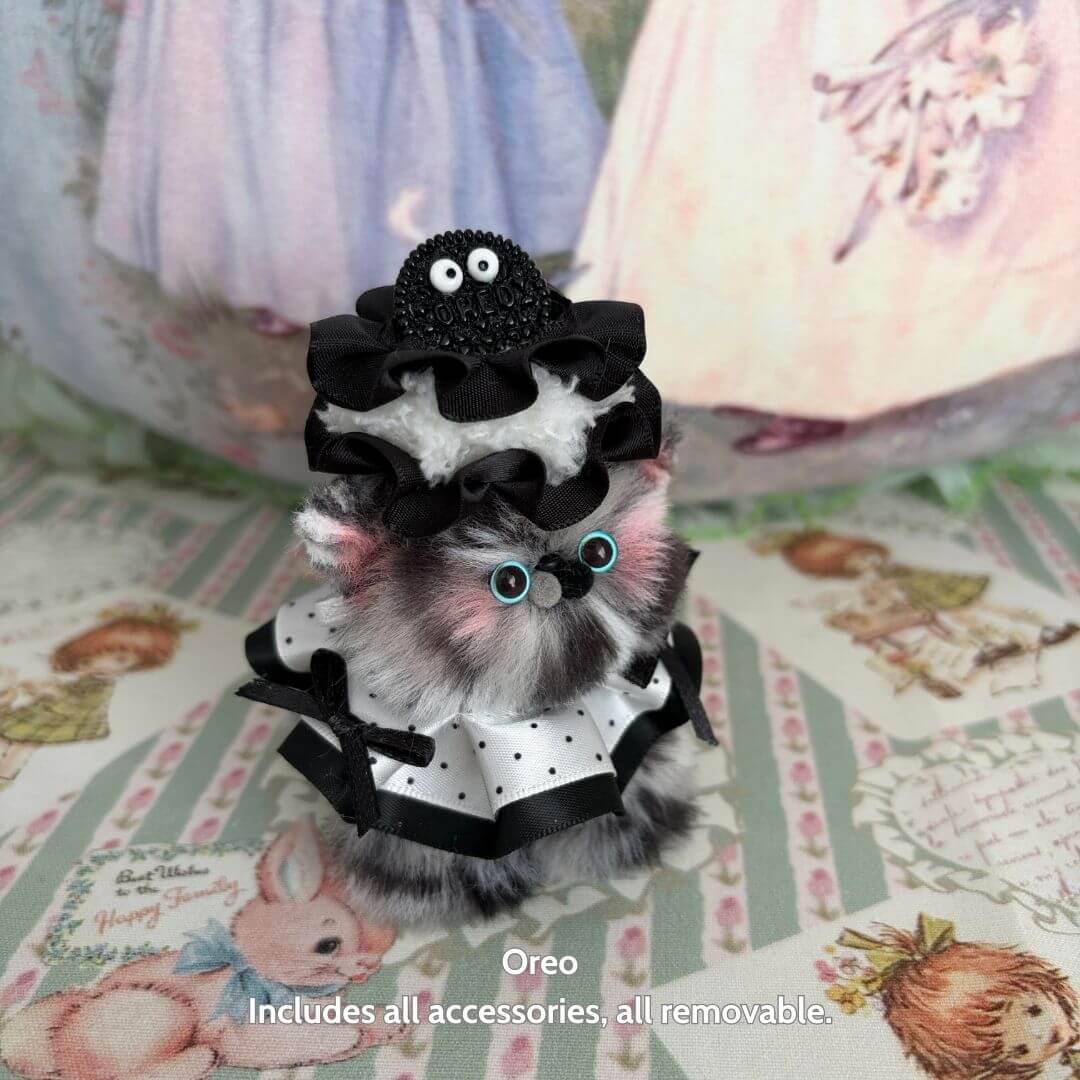 Handmade kitten Oreo with black and white dessert-themed accessories, fluffy faux fur, and cute blue eyes, Sweet Treat Kitties.
