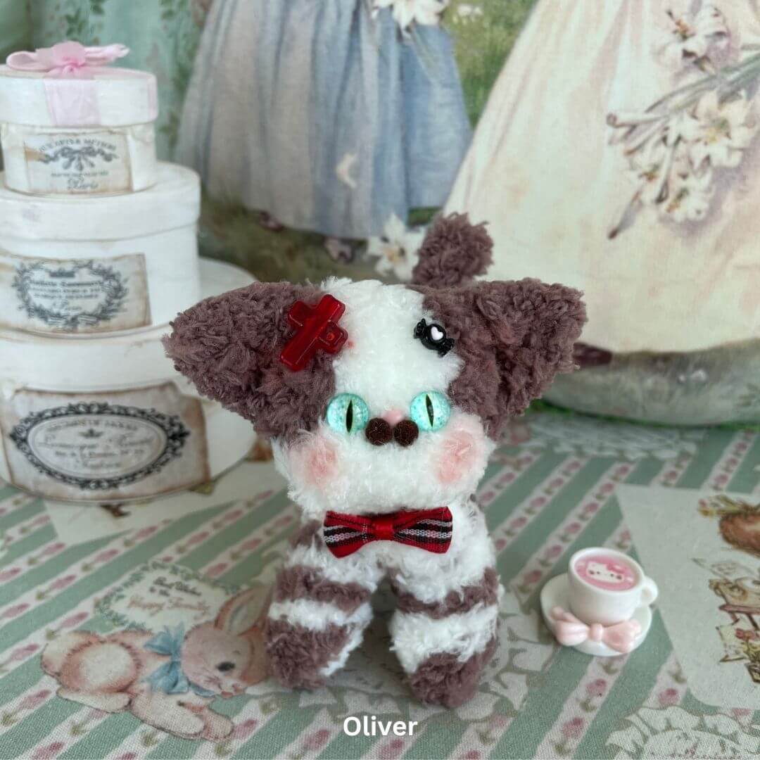Handmade plush Devon Rex kitten toy with big ears and velvet bow, positioned on a decorative background.