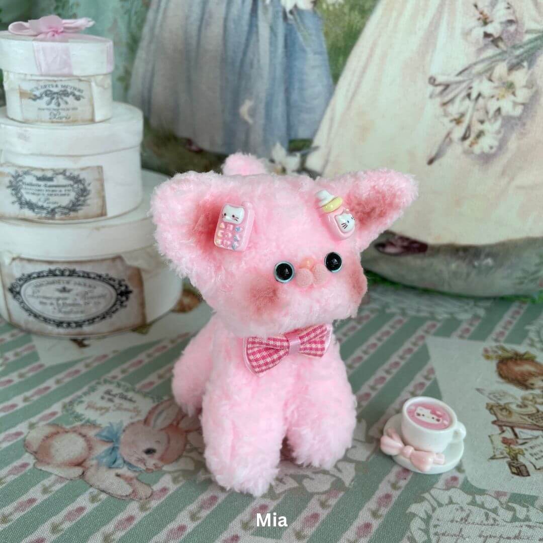 Pastel pink plush Devon Rex kitten with a bow and decorative accessories, inspired by the playful charm of real Devon Rex cats.