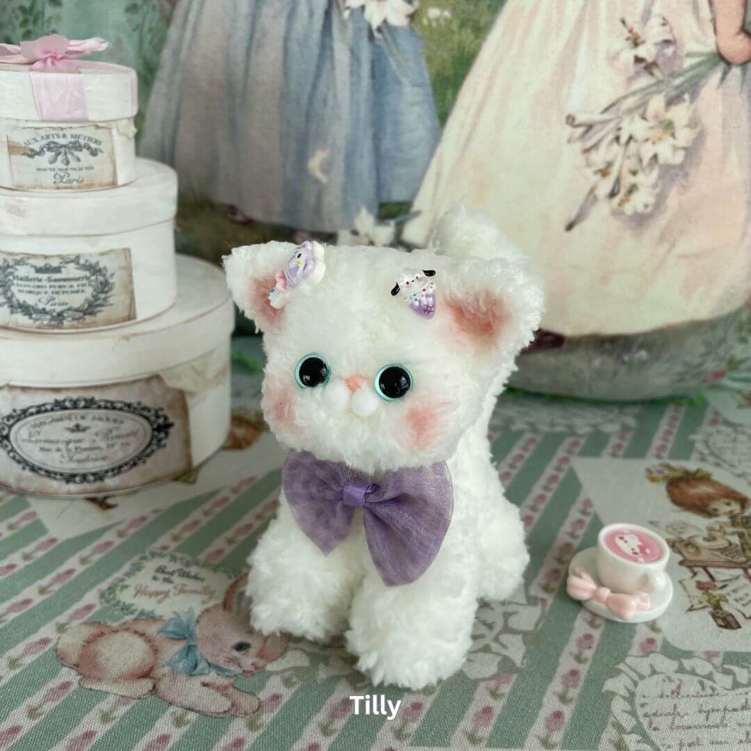 Handmade plush Devon Rex kitten toy with a purple bow, soft faux fur, and charming ears, surrounded by vintage decor.