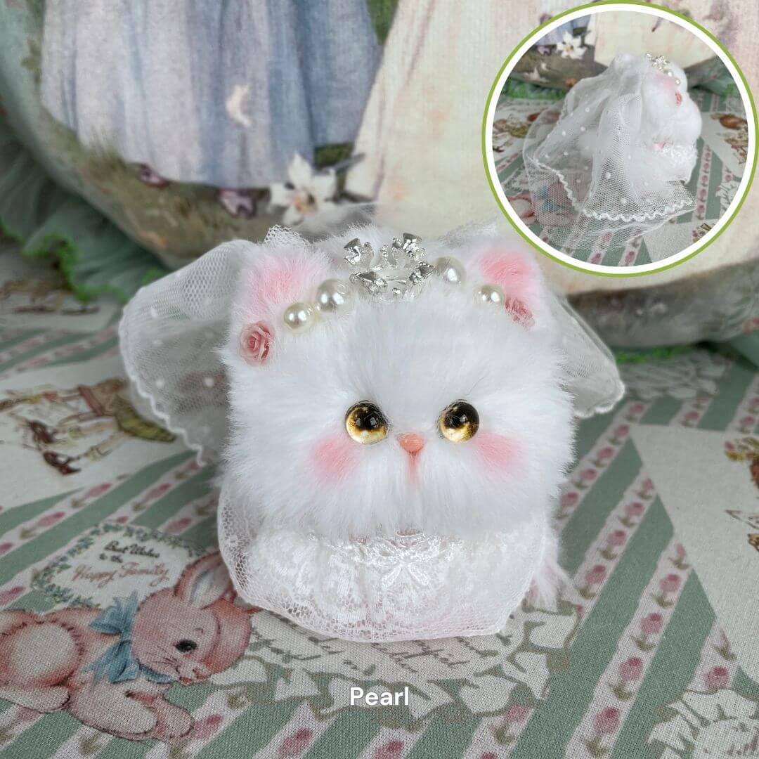 Handmade plush kitten toy with pearl tiara and lace veil, part of the Fairy Paws Collection, set in a whimsical meadow-themed backdrop.